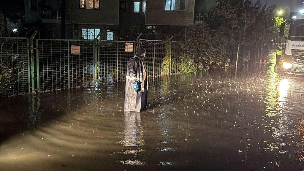 Woman in rain gear standing in flood water at night