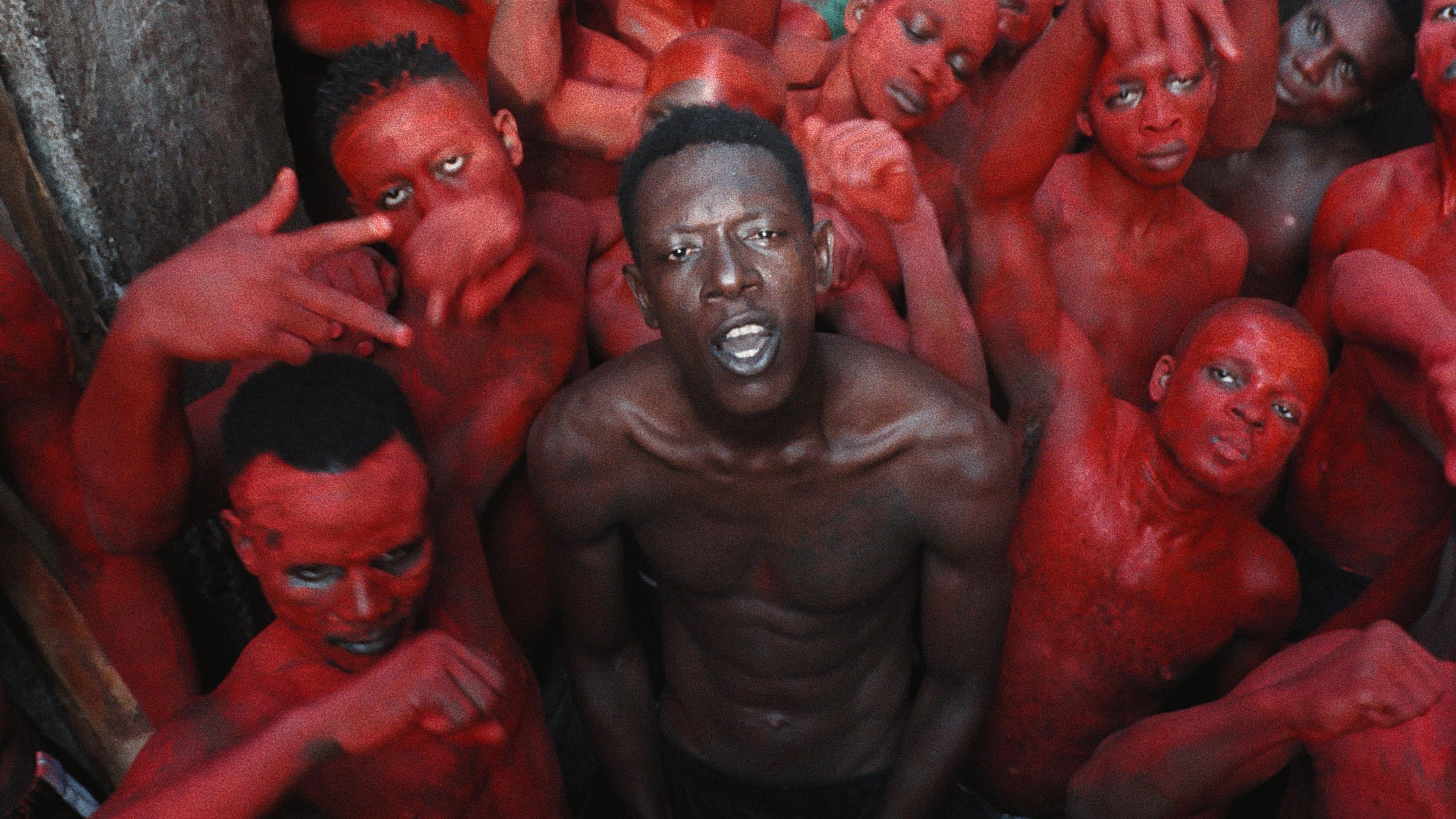 An inmate named Empereur stands in the centre of a group of young men, painted in red